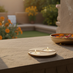 Two lit candles in a mdf tealight candle holder in a decorative holder on a stone surface with a blurred garden background.