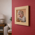 Wooden photo frame with a smiling baby holding a teddy bear against a red wall.