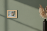 Wooden photo frame on a green wall with a baby photo inside, next to a vase with dried plants.