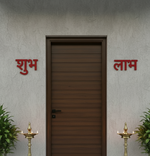 MDF Shubh Labh wall hanging decor in red color placed on both sides of main door with traditional lamps.