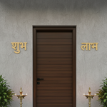 MDF Shubh Labh wall decor in golden color placed at entrance with plants and lamps for festive look.