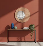 Decorative round mirror with floral patterns on a red wall above a console table.