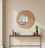Round decorative mirror with floral patterns on a beige wall above a wooden console table.
