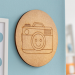 Unpainted round MDF pre-marked camera base with smiley lens design for DIY kids painting and craft.