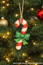 Hand-painted MDF candy cane ornament with red and white stripes and a green bow, hanging on a decorated Christmas tree with warm lights and baubles.
