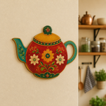 Colorful teapot-shaped MDF wall art with floral folk design mounted on a warm beige kitchen wall.