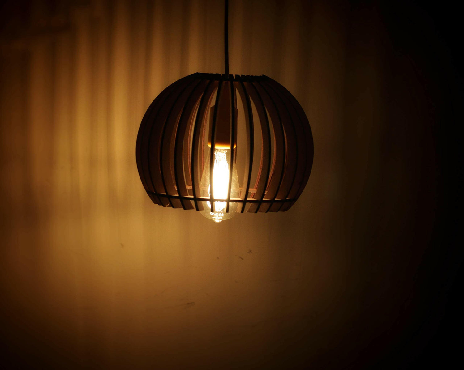 Matte black cage-style ceiling pendant lamp hanging with warm glowing bulb and cord
