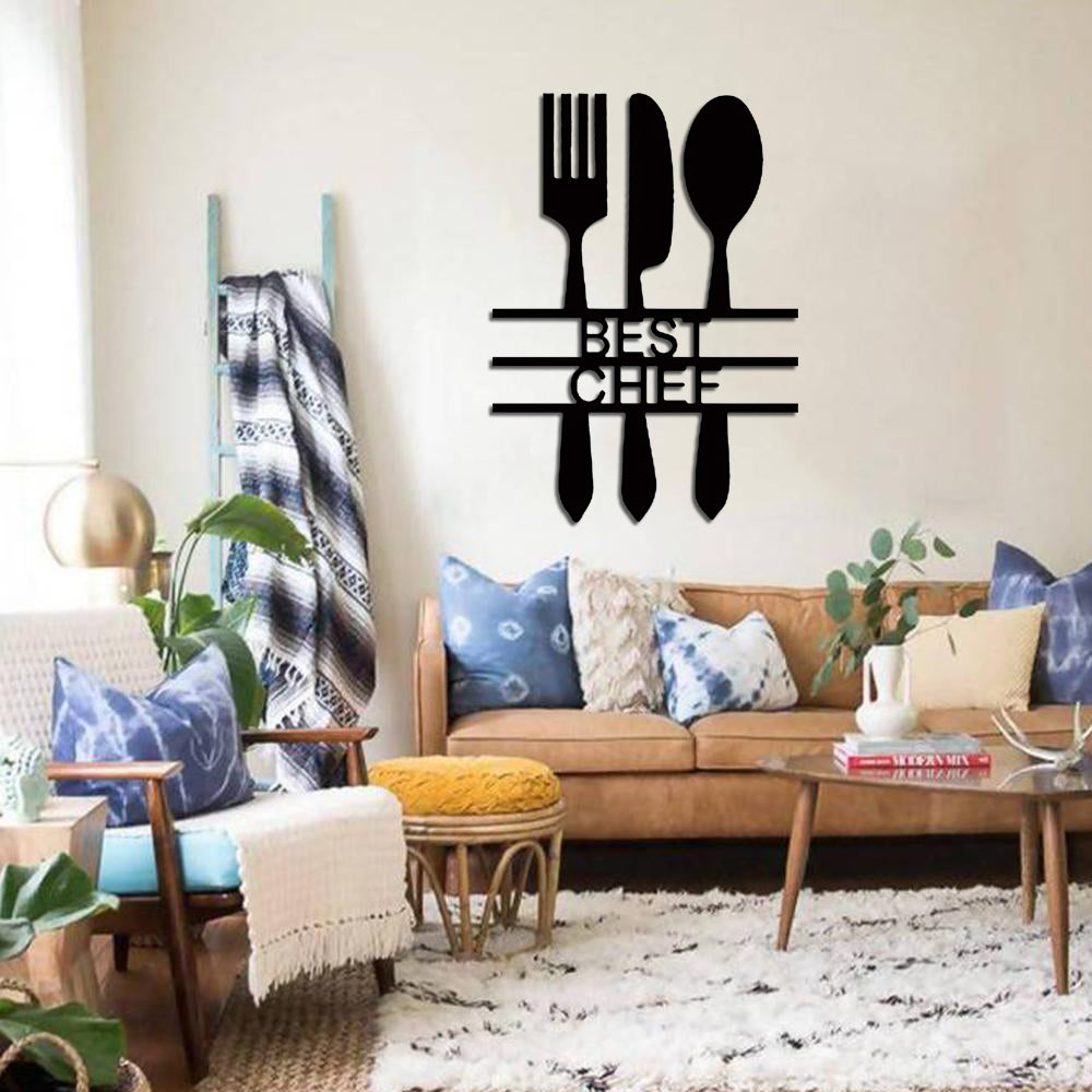 Black kitchen wall art featuring a fork, knife, and spoon design with the text 'BEST CHEF,' displayed on a wall in a cozy living room with a tan sofa, blue and white cushions, and a modern decor setup.