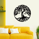 Round black wall art featuring an intricate tree of life design with visible roots, mounted above a yellow sofa adorned with white cushions.