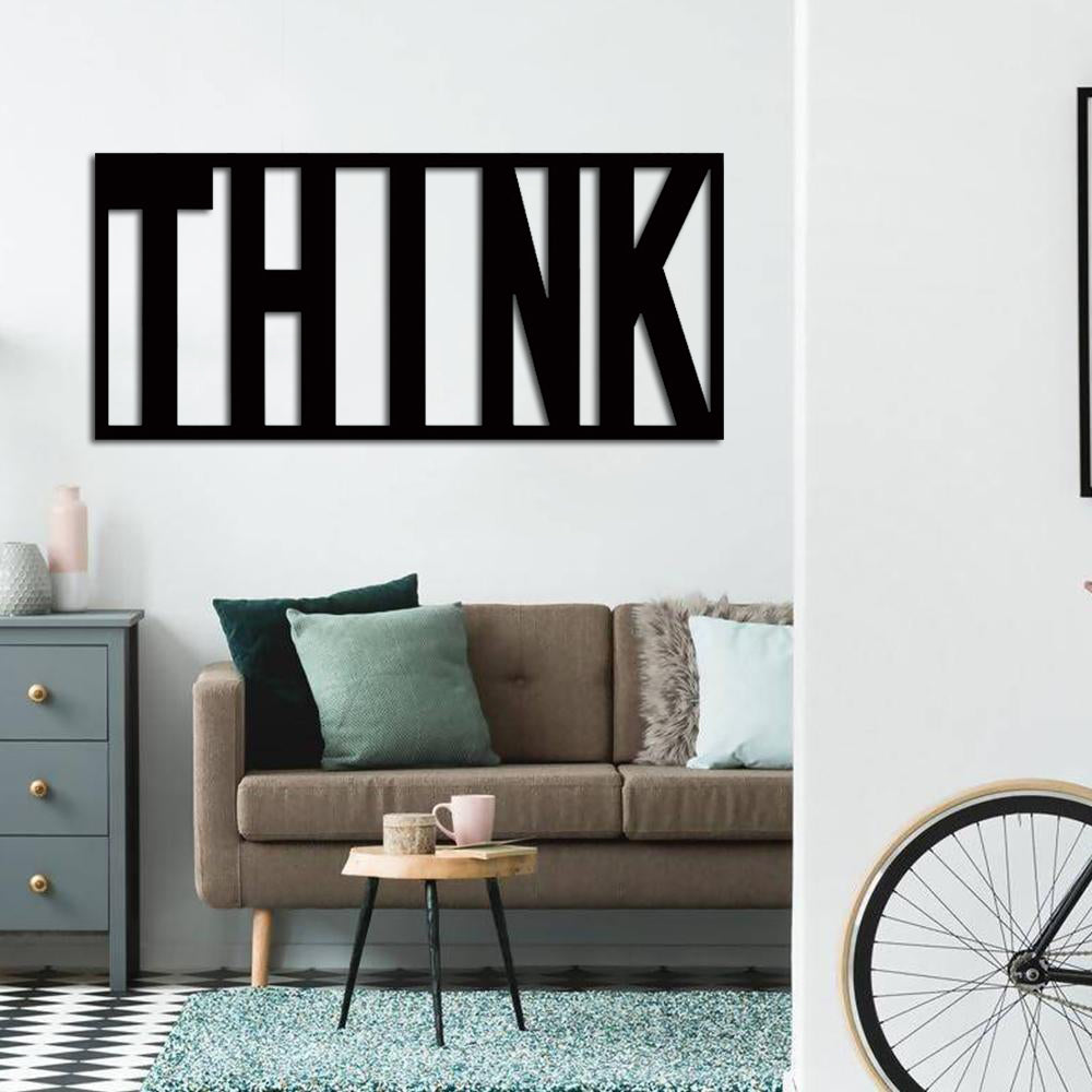 Black MDF wall art with the word "THINK" in bold typography, mounted on a white wall above a modern living room setup featuring a sofa, cushions, and a side table.