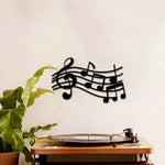 Black musical notes wall art featuring a treble clef and flowing staff lines displayed above a turntable setup.