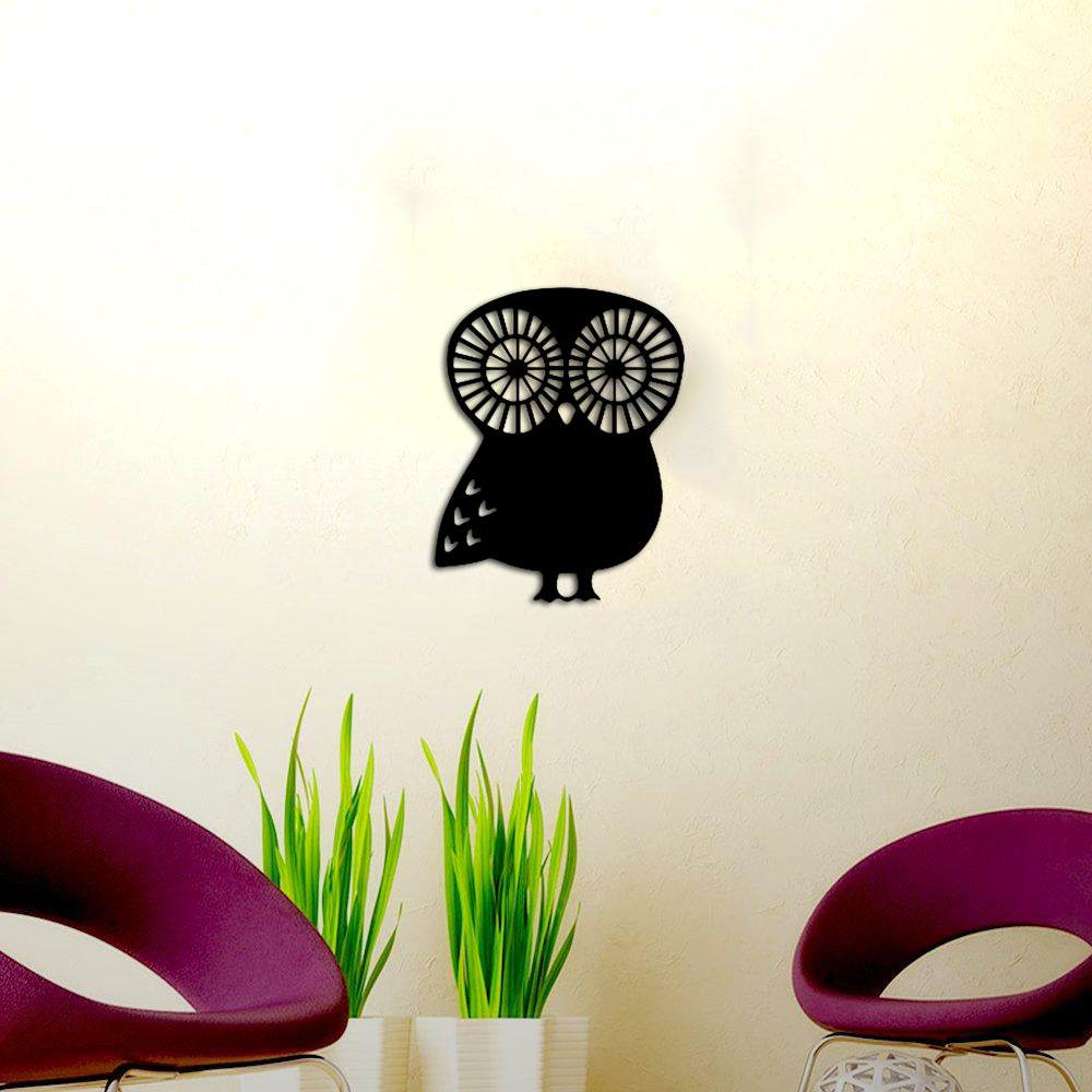 Black owl-shaped wall art with intricate circular eye patterns mounted on a light beige wall, surrounded by modern decor elements.