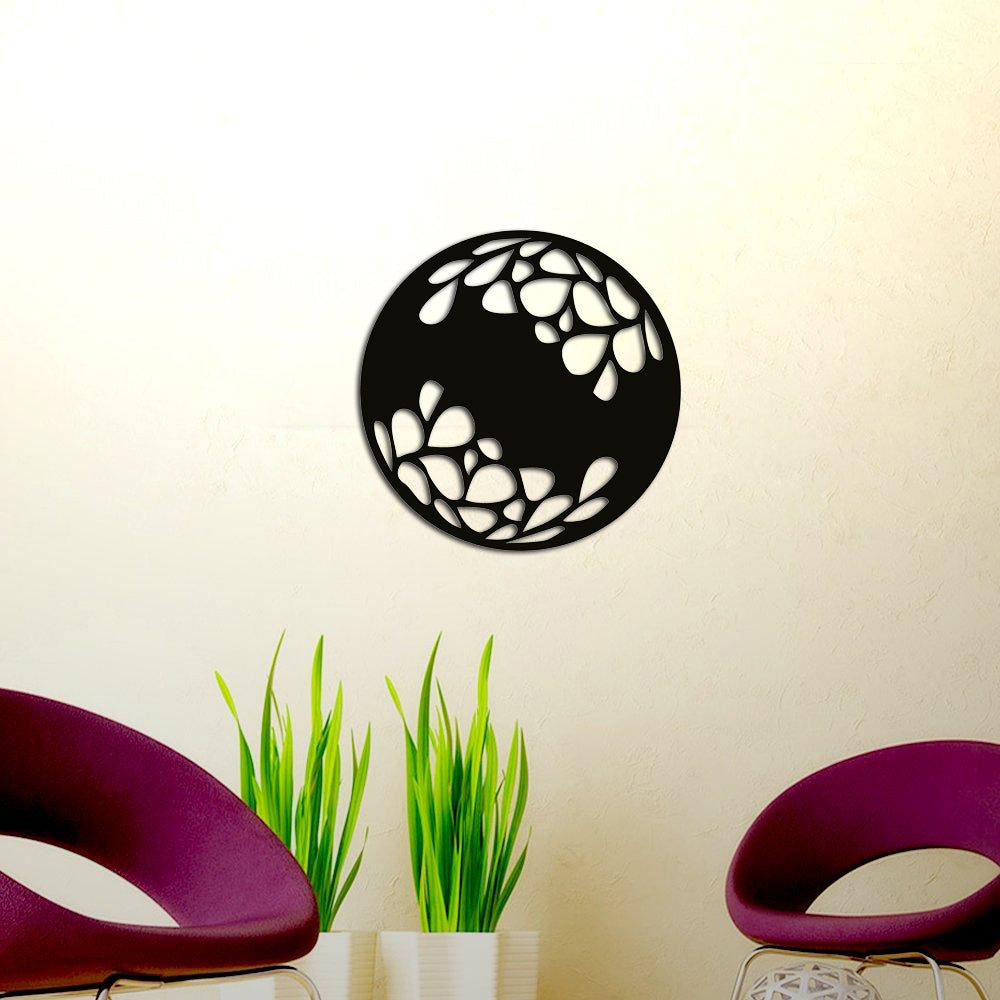Circular black MDF wall art with abstract leaf-inspired cutout patterns, mounted on a cream-colored wall, adding a modern touch to a space with purple chairs and green potted plants