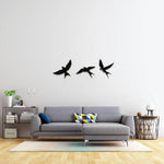 Black free bird wall art featuring three silhouettes of birds in flight, mounted on a white wall above a modern grey sofa