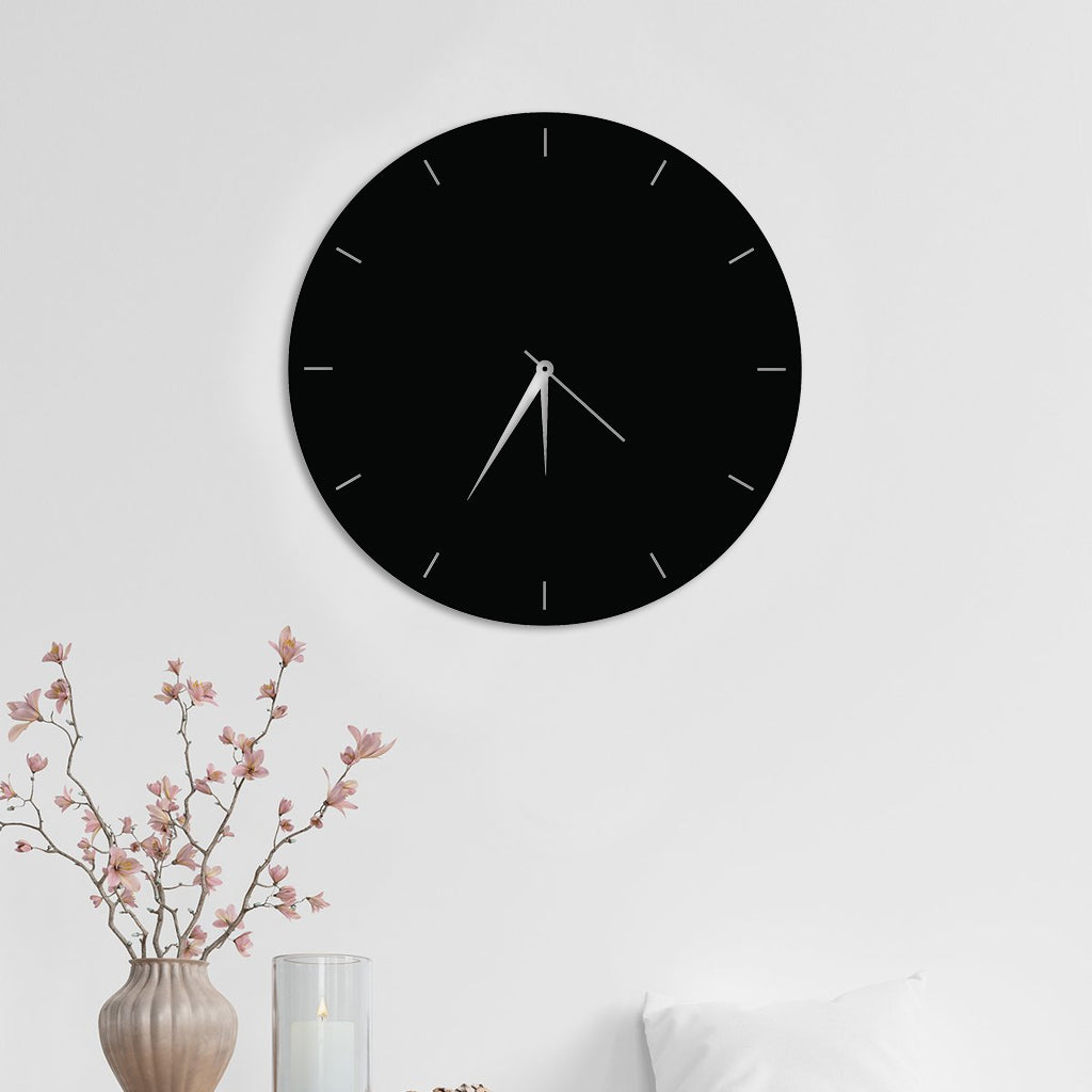 Minimalist black MDF wall clock with white hands mounted on a white wall, complementing a modern interior with floral decor.