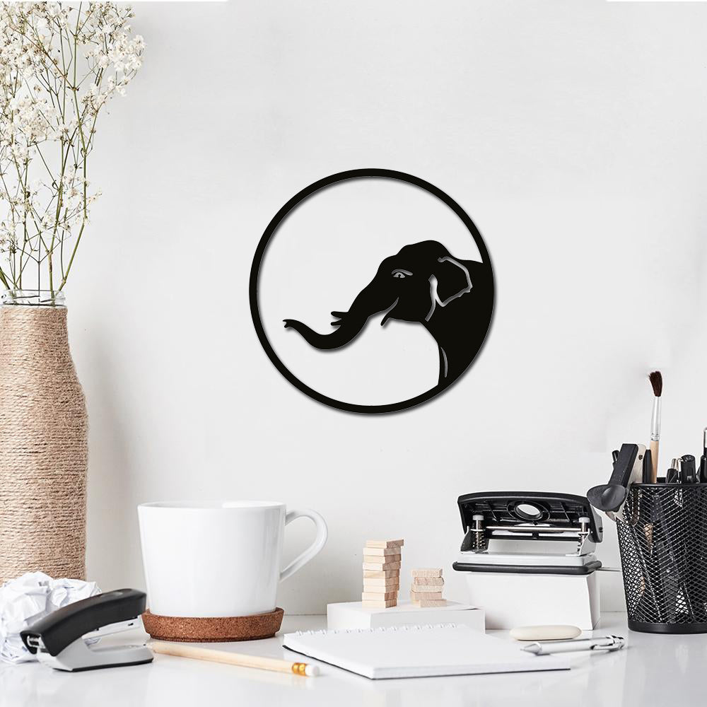 Round black MDF wall decor featuring a minimalist silhouette of an elephant head with a raised trunk, mounted on a white wall above a workspace.