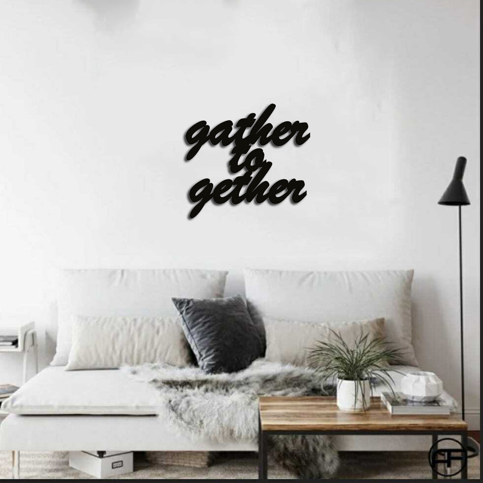 Black 'Gather Together' wall decor sign mounted on a white wall above a cozy sofa with decorative pillows and a wooden coffee table.