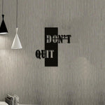 Motivational wall art with the phrase 'Don't Quit' displayed on a textured gray wall in a modern workspace.