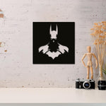 Batman wall decor featuring a sleek black and white silhouette design, mounted on a white brick wall above a minimalist desk with decorative items and a vintage camera.